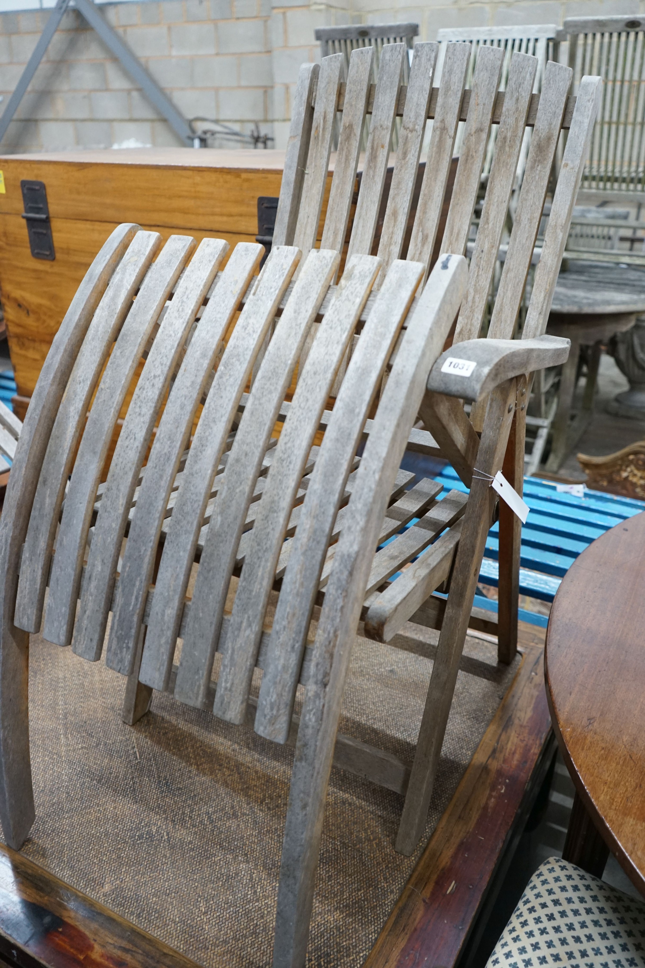 A pair of weathered teak folding reclining garden elbow chairs with footrests and seat pads